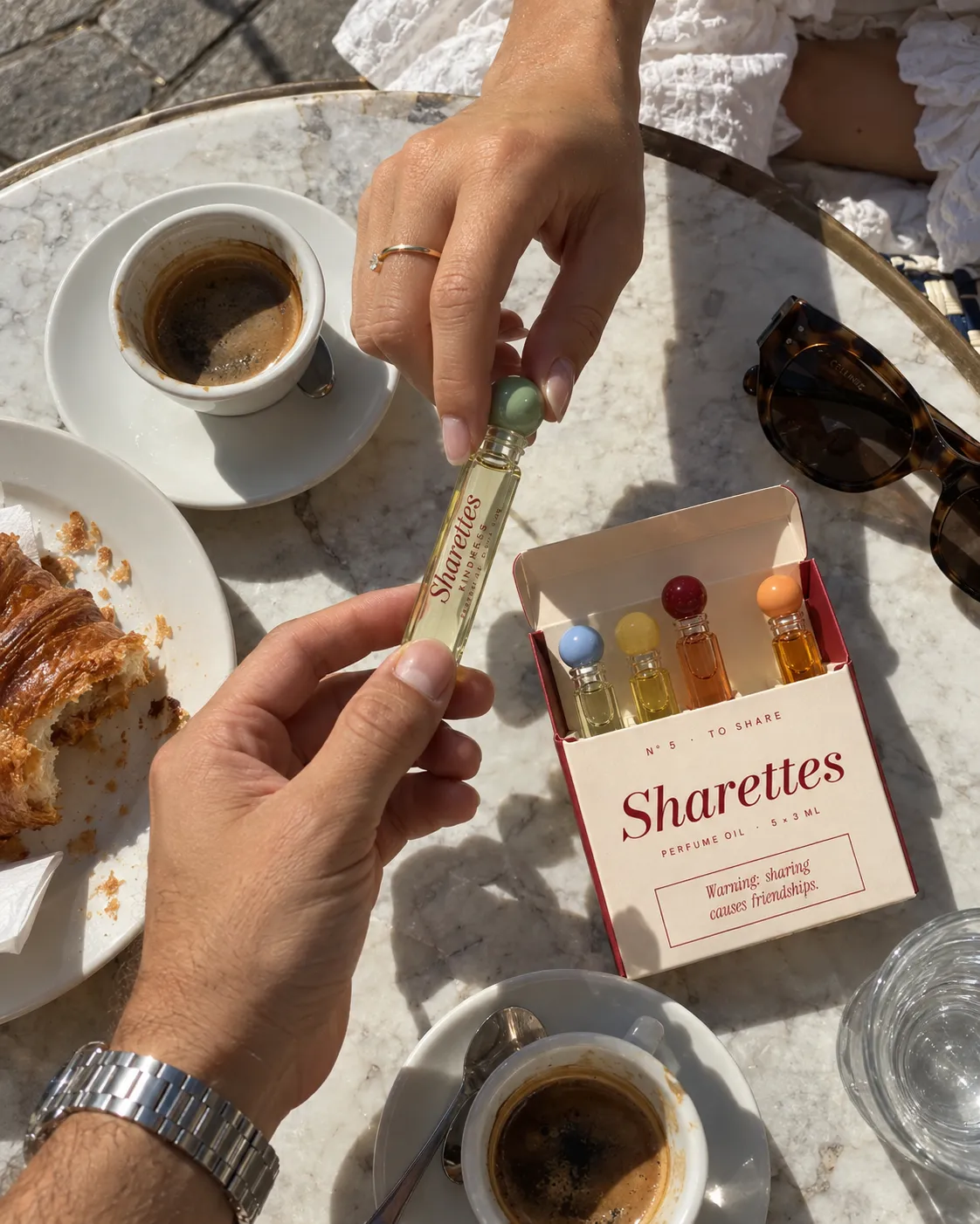 A hand offering the cherry tube from an open Sharettes pack at a café table